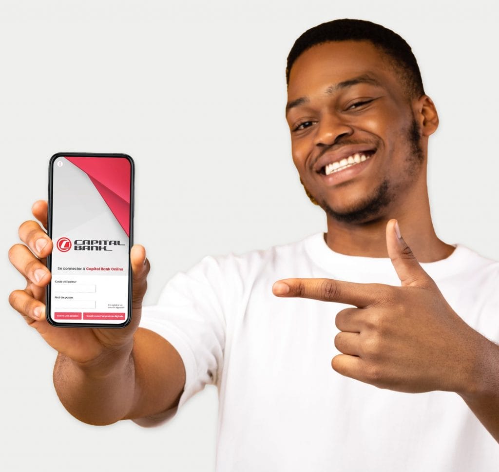 Jeune homme souriant et pointant du doigt son téléphone portable montrant Capital Bank Online, le service de banque en ligne de Capital Bank